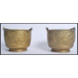 A pair of Chinese brass bowls having a relief dragon decoration with swing handles a top. Measures