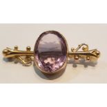 A 9ct gold and amethyst bar brooch with pin verso, The large oval faceted amethyst with scrolled bar