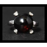 A hallmarked 9ct white gold, garnet and white stone ring set with a garnet cabochon with four accent