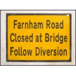 A 20th century road works diversion sign on yellow ground with black lettering reading Farnham