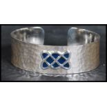 A sterling silver arts and crafts style bangle bracelet having a hammered design with an enamel