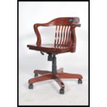A 20th century stained beech captains office chair raised on a wheeled five point base with
