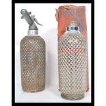 Two vintage oversized Soda Syphons by Sparklets, both with wire mesh covers and one retaining its