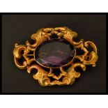 A large gold tone metal and amethyst brooch having a large central faceted stone with scrolled mount