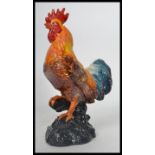 A vintage style cast iron figurine of a cockerel raised on a naturalistic base being painted.