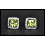 A pair of sterling silver and CZ stud earrings of square form having central peridot stones.