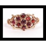 A hallmarked 9ct gold and garnet cluster ring having an antique style scroll setting. Hallmarked