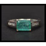 A 14ct white gold emerald and diamond ring having a central faceted emerald with diamond encrusted