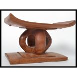 A 20th century African hardwood tribal stool / pillow neck rest having an angular seat raised on