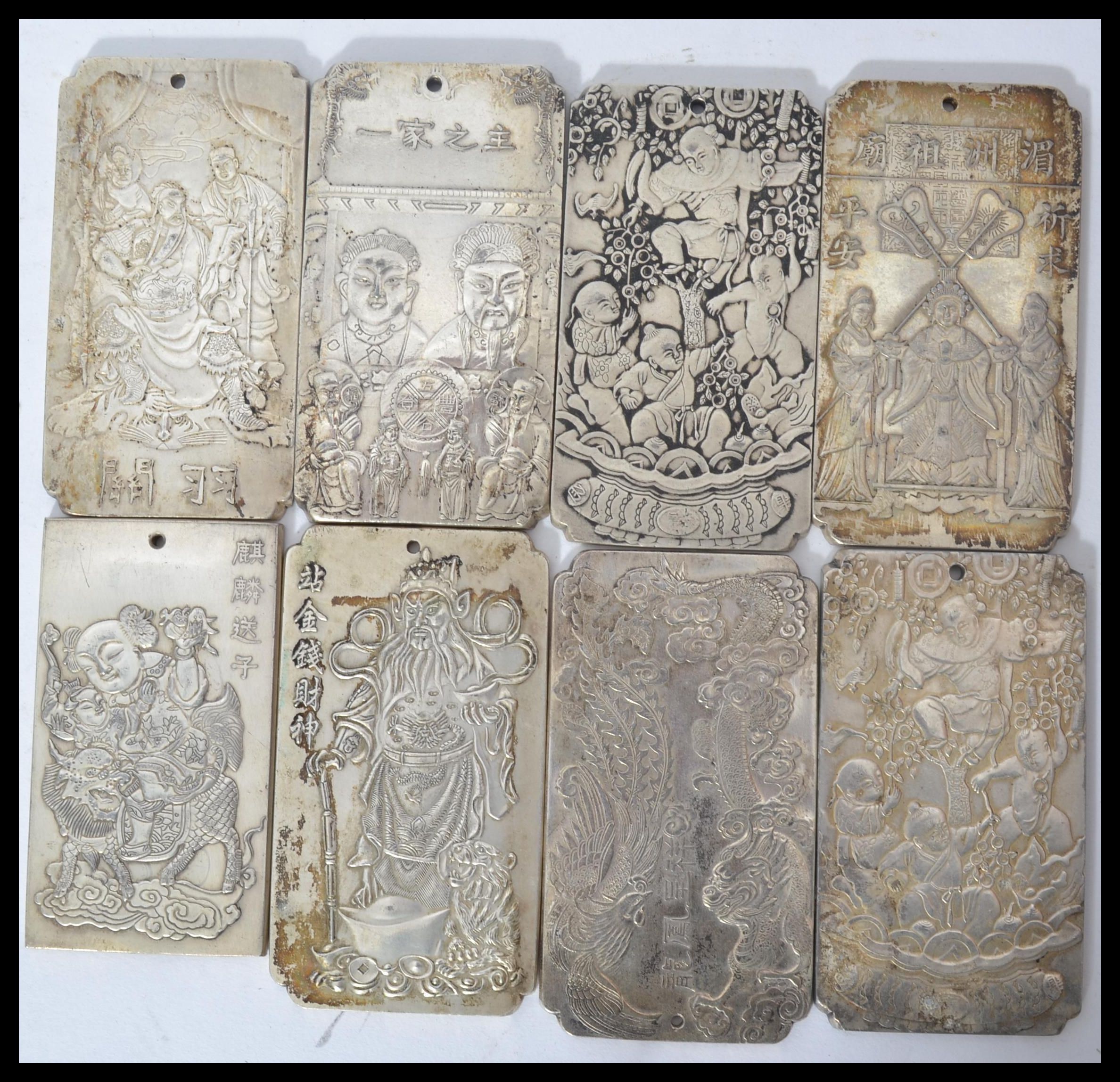 A collection of eight Chinese white metal amulet / scroll weights, cast in relief with various