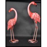 A pair of patterned metal garden ornament flamingos having a painted pink feathered finish.