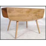 A retro mid 20th century beech and elm Ercol drop leaf dining table being raised on squared legs