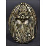 A brass vesta case in the form of a bat hiding within its wings.