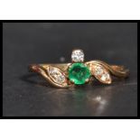 An 18ct gold diamond and emerald crossover ring having a central emerald stone with diamond leaves