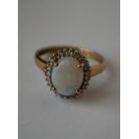 A hallmarked 9ct gold ring set with a central opal surrounded by a diamond halo. Diamonds approx