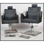 A pair of contemporary retro style minimalist chrome salon chairs being raised on chrome bases