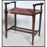 An Edwardian mahogany piano stool having upholstered seat with hinged top flanked by scrolled