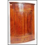 A late Georgian wall hanging bow fronted corner cabinet in mahogany having twin doors to reveal a