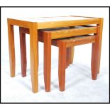 A retro teak wood Danish inspired nest of three tiled top tables, raised on square legs united by