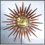 A vintage mid century teak wood sunburst wall clock. The gilded dial with roman numeral chapter ring