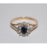 A hallmarked 9ct gold cluster ring  having a central oval cut blue sapphire surrounded by a CZ halo.