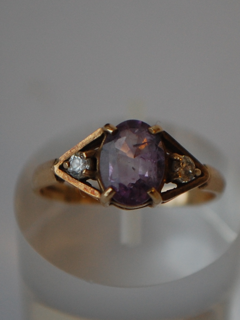 A hallmarked 9ct gold three stone ring set with a central oval cut purple stone flanked by two white