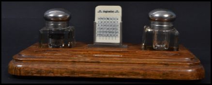 A vintage early 20th century desk top pen rest and twin capstan inkwell calendar compendium.