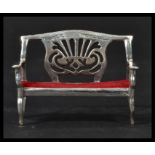 A sterling silver antique style miniature model of a lyre back sofa with red baize cushion. Weighs