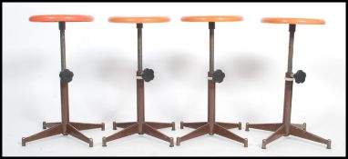 A set of four vintage 20th century retro stools having orange circular tops raised on adjustable