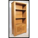 A contemporary chunky oak upright bookcase cabinet with cupboard to the base having shelves above.