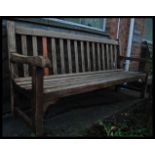 A 20th century teak wood garden bench having slatted seat and back rest flanked by shaped elbow