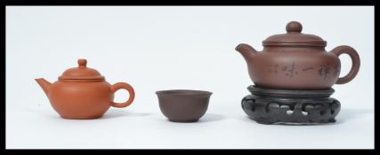 A vintage 20th century Yi Xing red clay Chinese tea pot and cup on wooden socle base along with