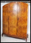 A 1930 Art Deco bow front triple wardrobe armoire. Raised on a cabriole legs with pad foot plinth