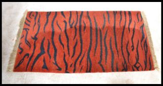 A 20th century Tibetan style tiger rug. Orange ground with black tiger striping, tassled ends