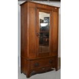 An  Edwardian Arts & Crafts light oak wardrobe  having a plinth drawer base with central mirror door