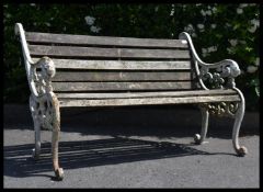 A vintage well weathered two seater garden bench seat with scrolled lions head bench ends. In the