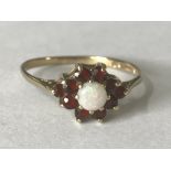 A hallmarked 9ct gold opal and garnet cluster ring. The central round cut opal having a halo of