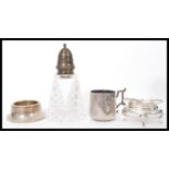 A group of four silver condiment items to include a cut glass silver lidded pepperette, silver