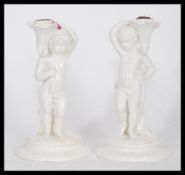 A pair of 19th century ceramic table taper candlesticks in the form of cherubs holding cornucopia