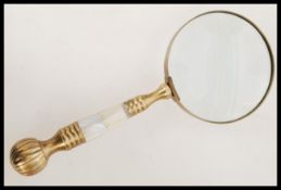 A 20th century hand held magnifying glass having a brass handle with inset mother of pearl panels.