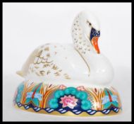 A Royal Crown Derby ceramic paperweight in the form of a nesting swan complete with stopper.