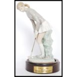A Lladro ceramic figurine of a lady golfer with putter ( 4851 ) raised on a wooden base with applied