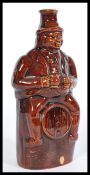 A 19th century salt glazed stoneware bottle flask depicting a Victorian man sitting on a barrel with