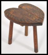 A 19th century Arts & Crafts dark wood milking stool, with a heart form top having a carved jack