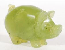 A Chinese carved green jade figurine of a pig havi