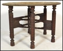 A 19th century Anglo- Colonial brass topped table with a circular legged folding ornate carved