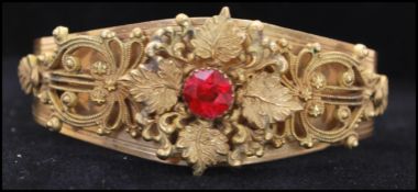 A Victorian gold tone bangle with red paste stone and filigree work. Measures 2.5 inches in