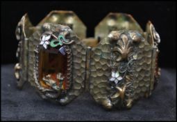 A Czech Gablonz planished 6 panel metal and enamel bracelet set with amber glass and decorated