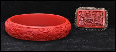 A 1930s Art Deco carved cinnabar brooch in a white metal mount marked China together with a cinnabar