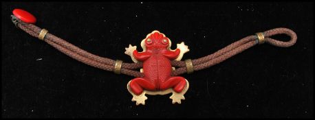 A 1940s bakelite figural bracelet strung with a red carved bakelite frog set on a brass mount with